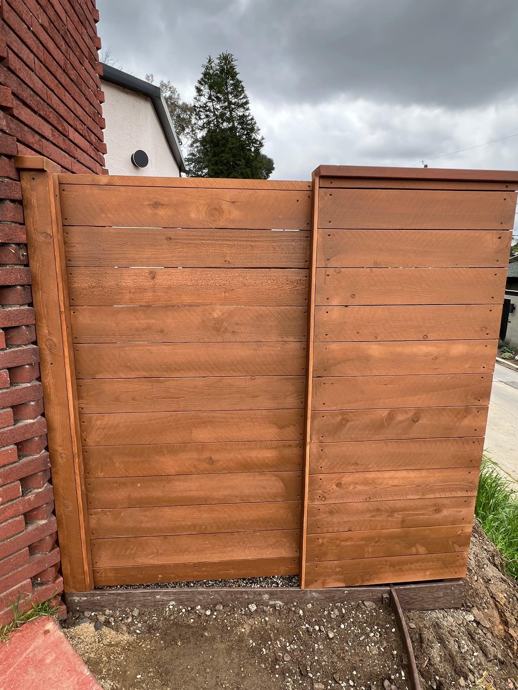 Redwood gate with Z-brace and black hardware next to a brick wall