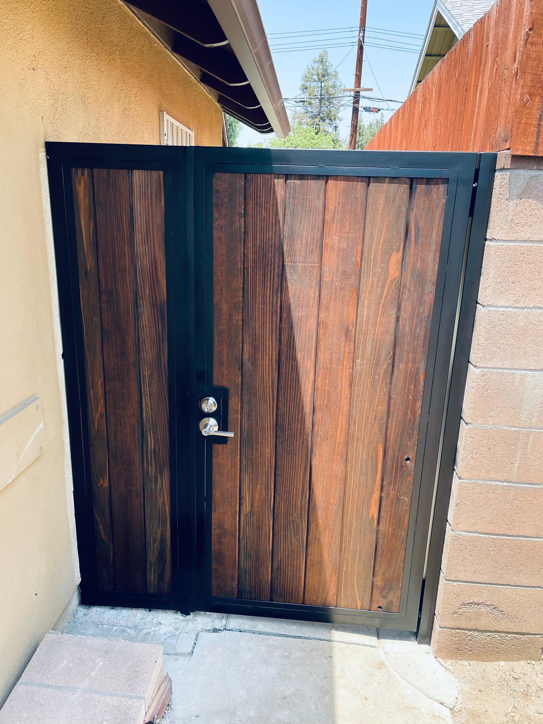Custom pedestrian gate with dark wood panels, black metal framing, and modern locking hardware