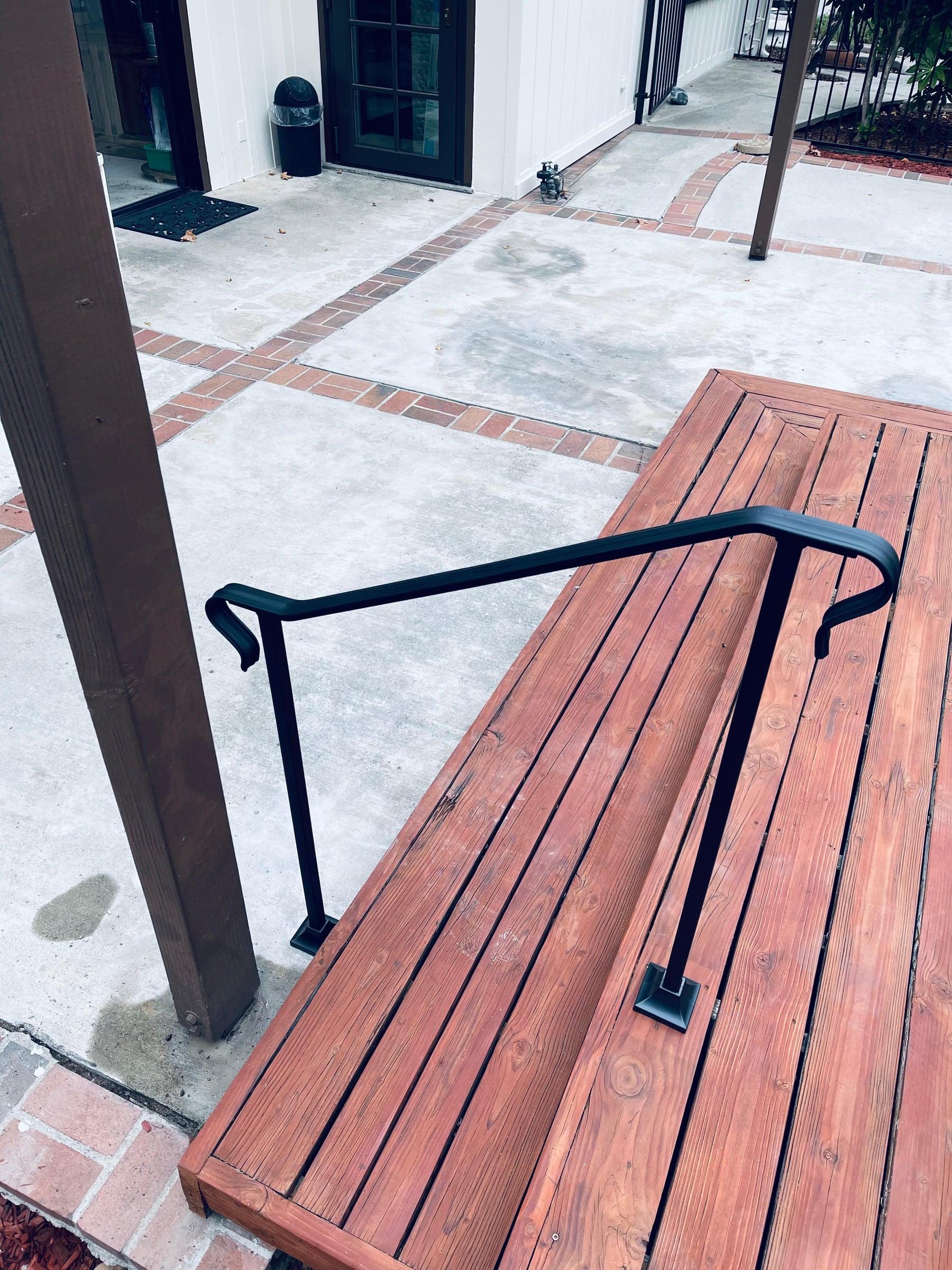 Custom black iron handrail installed along a wood deck staircase