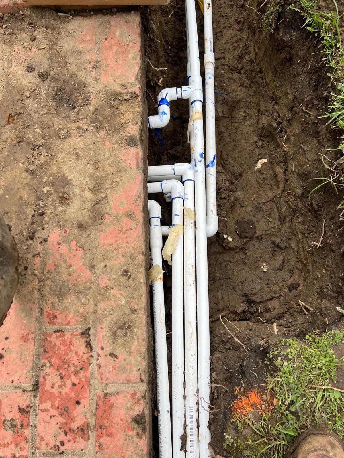 New PVC irrigation lines laid in a trench along a brick planter edge
