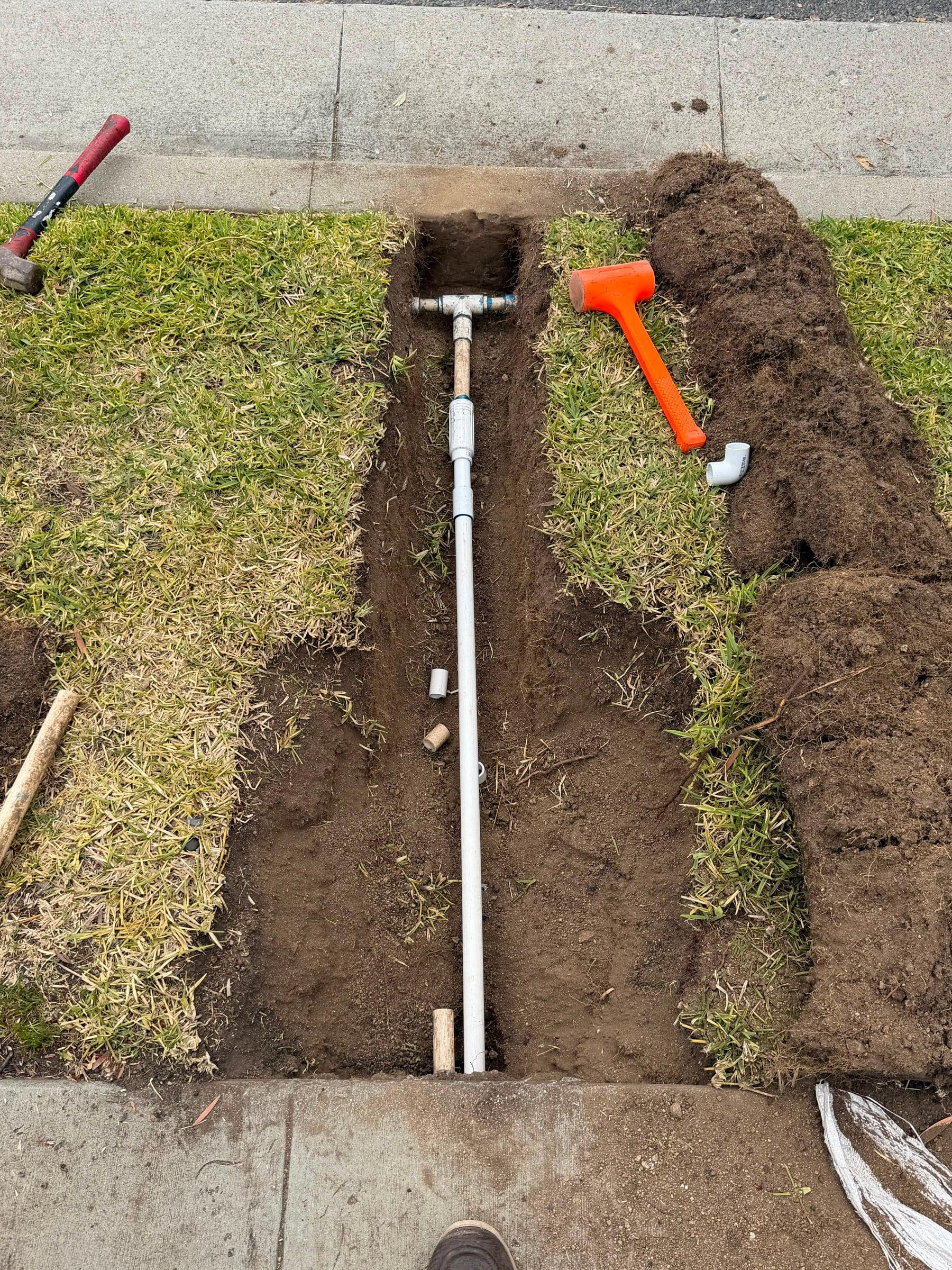 PVC irrigation main line trenched along a sidewalk edge