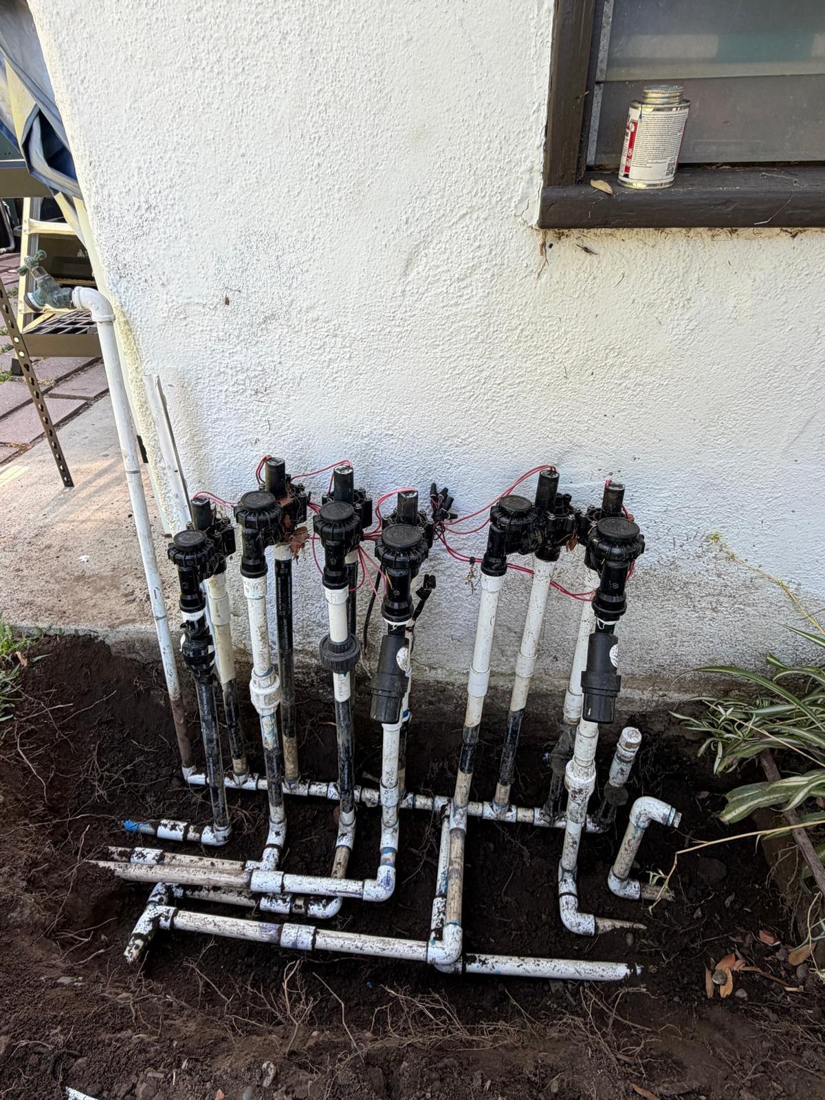 Manifold of new anti-siphon valves along a stucco foundation