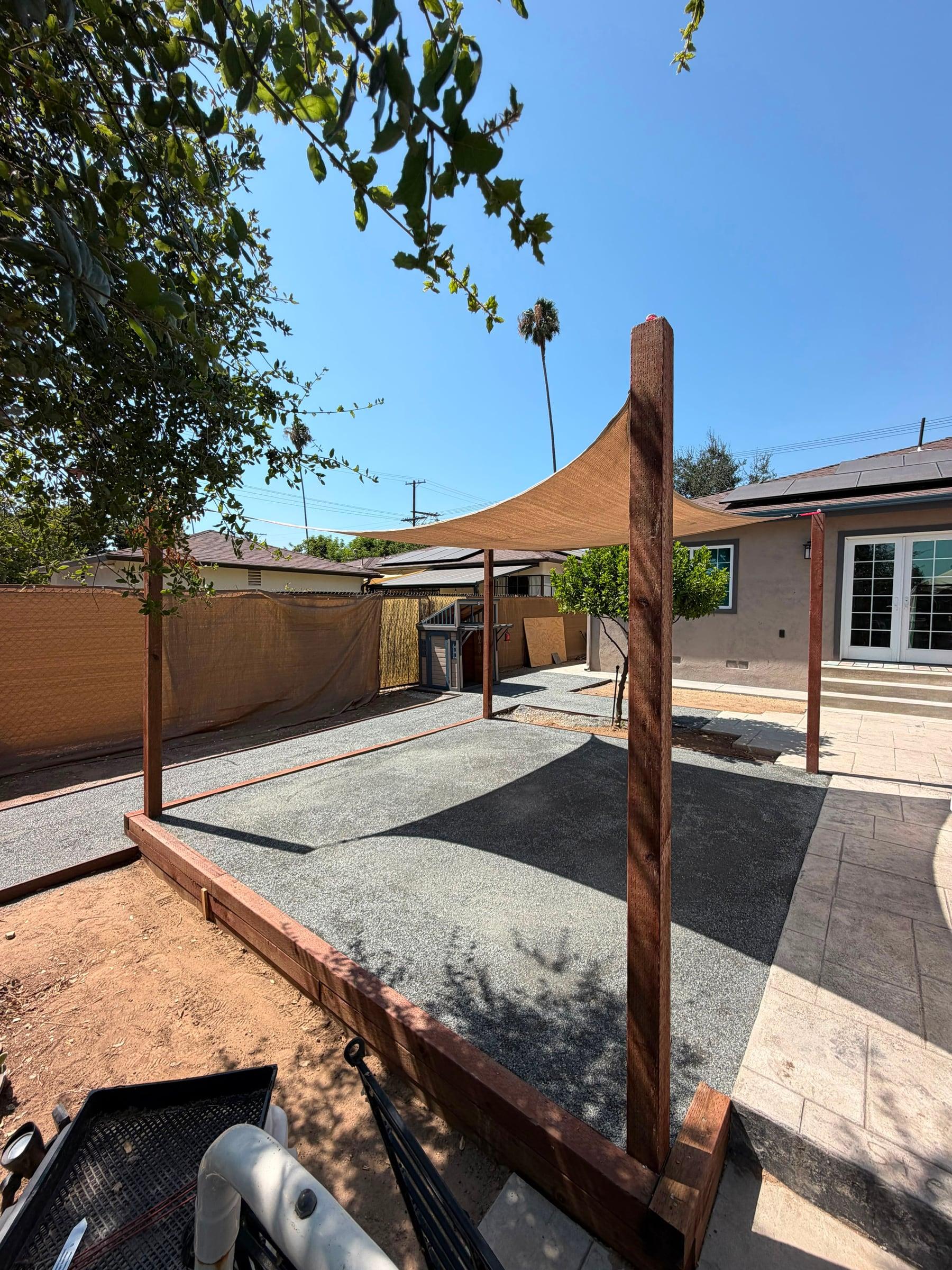 Backyard gravel patio with a shade sail and citrus tree