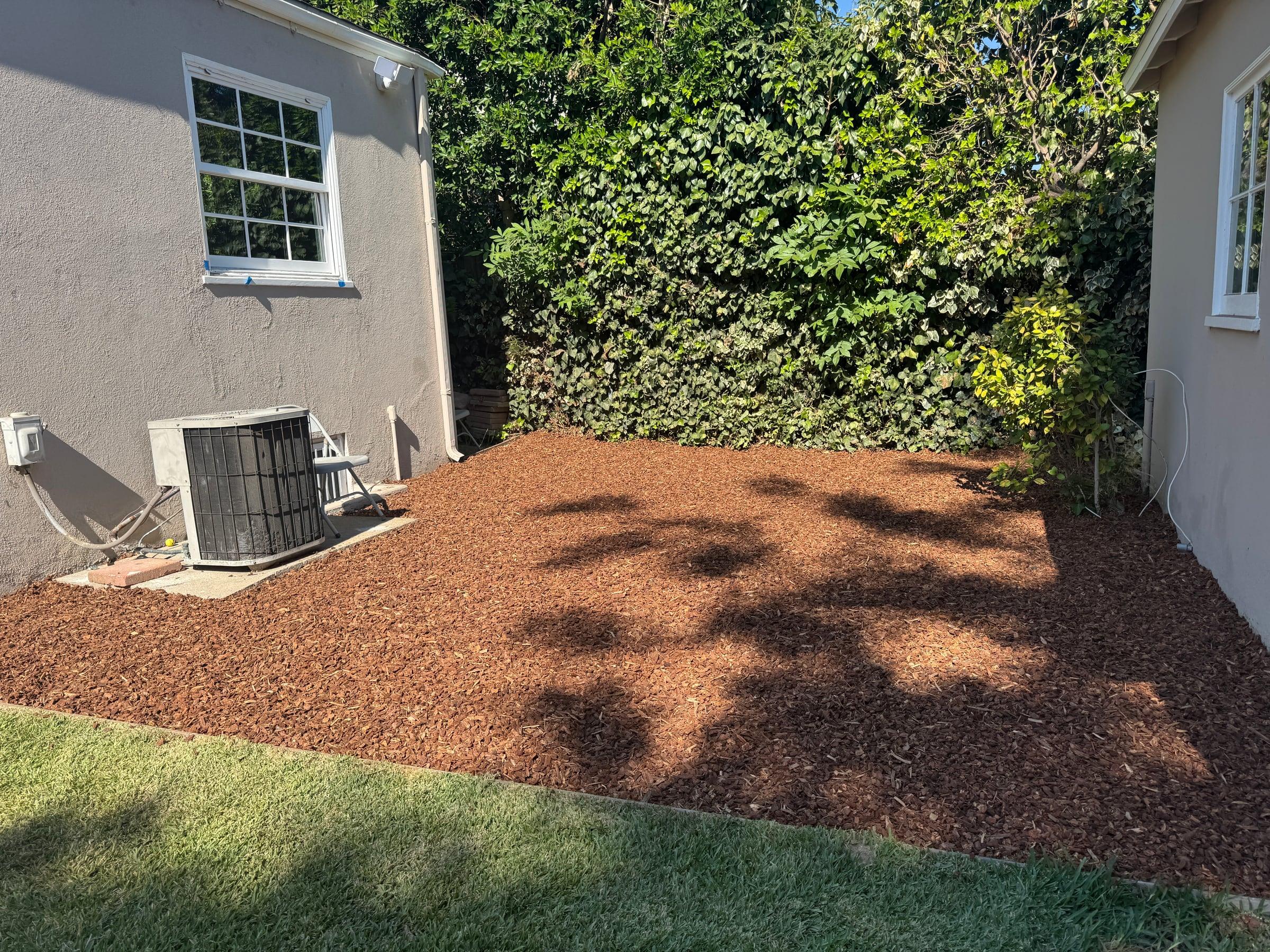 Bark mulch bed installed beside an outdoor AC unit