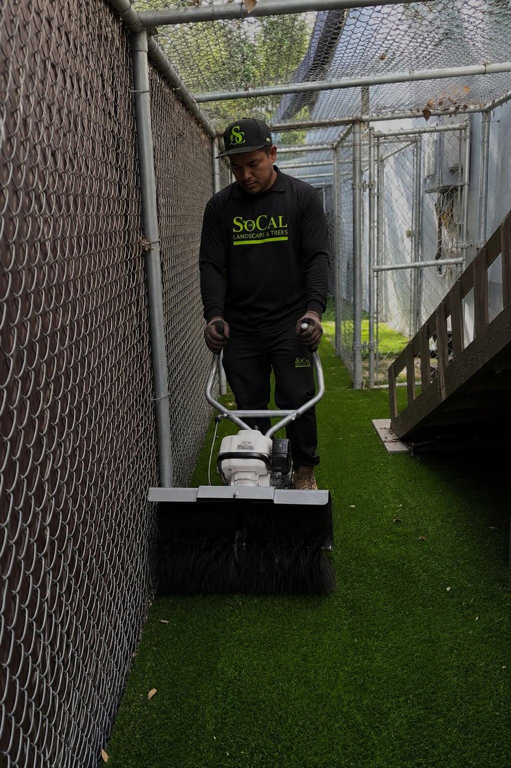 Crew member grooming artificial turf in a dog run area